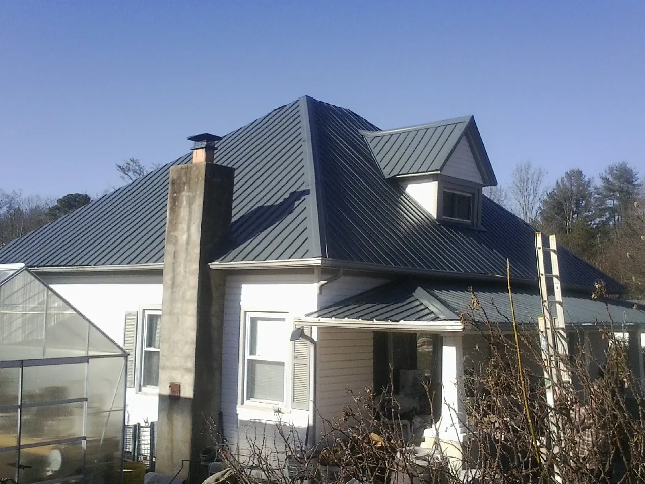 Dark blue standing seam metal roof on a white farmhouse with dormer — Slate & Tile Roof Repair by Roofing Brothers in Sweeny