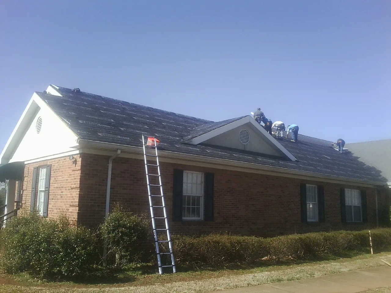 Crew tearing shingles off a brick ranch roof with a ladder set — Emergency Roof Repair work by our crew in Sweeny
