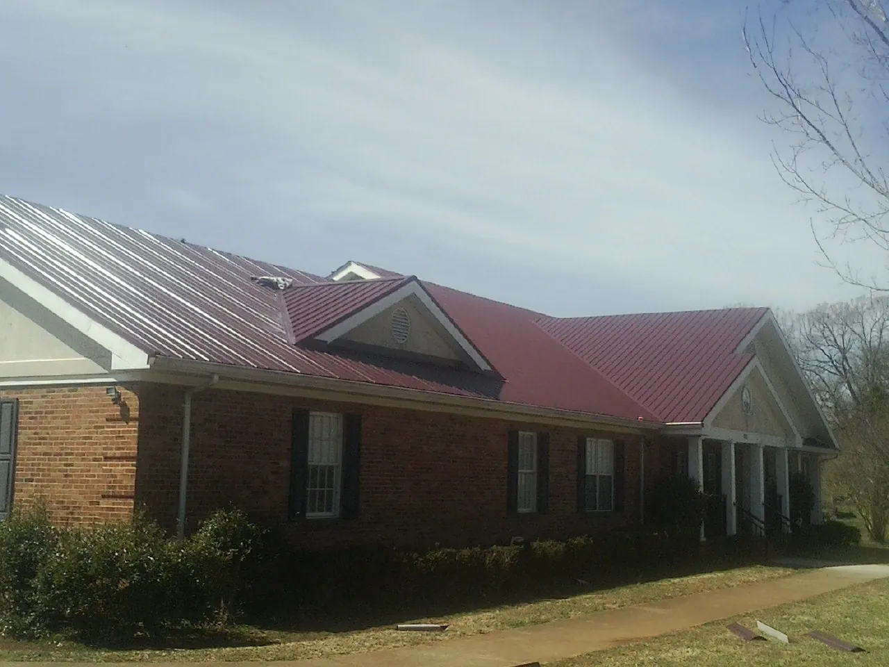 Red metal roof with gabled entries on a long brick building, from a Hail Damage Roof Repair job in Sweeny