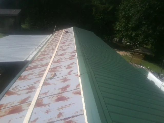 Old rusted panels beside newly installed green metal roofing — Wind Damage Roof Repair by Roofing Brothers in Sweeny