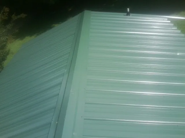 New green metal panels meeting at the ridge of a roof — Flat Roof Repair work by our crew in Sweeny