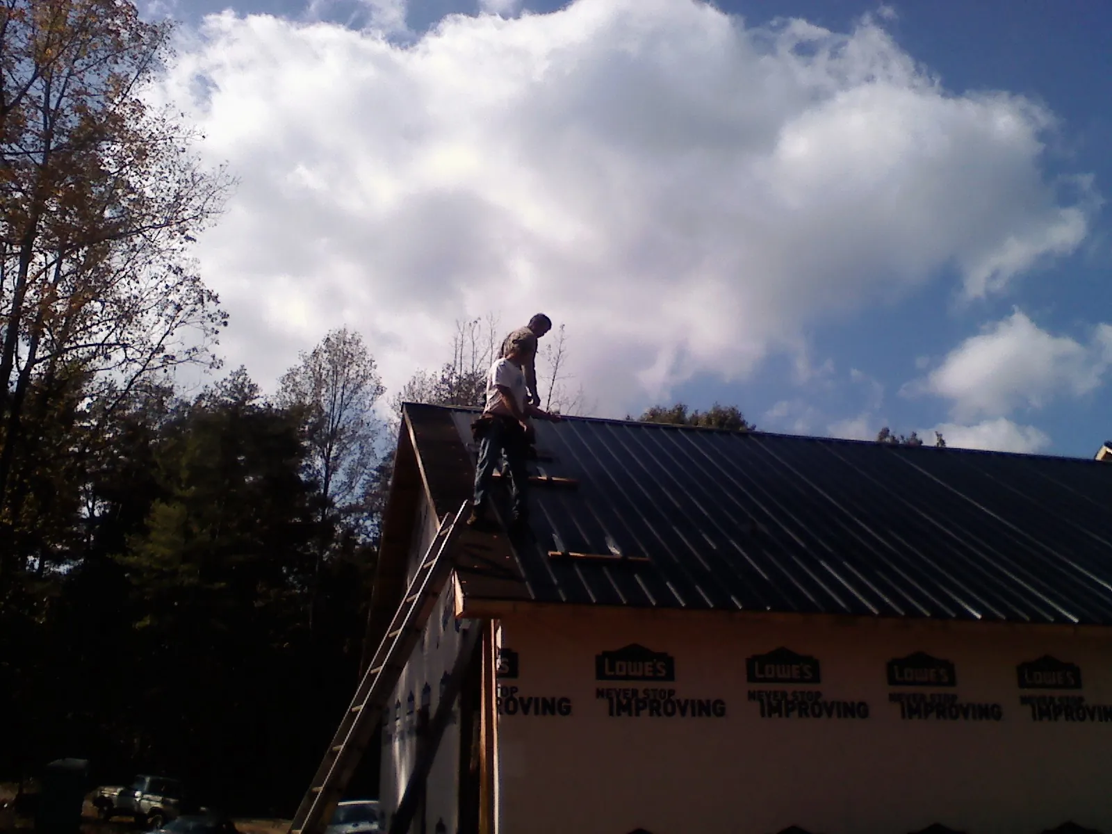 Roofer fastening dark metal panels high against a cloudy sky, from a Roof Inspection job in Sweeny