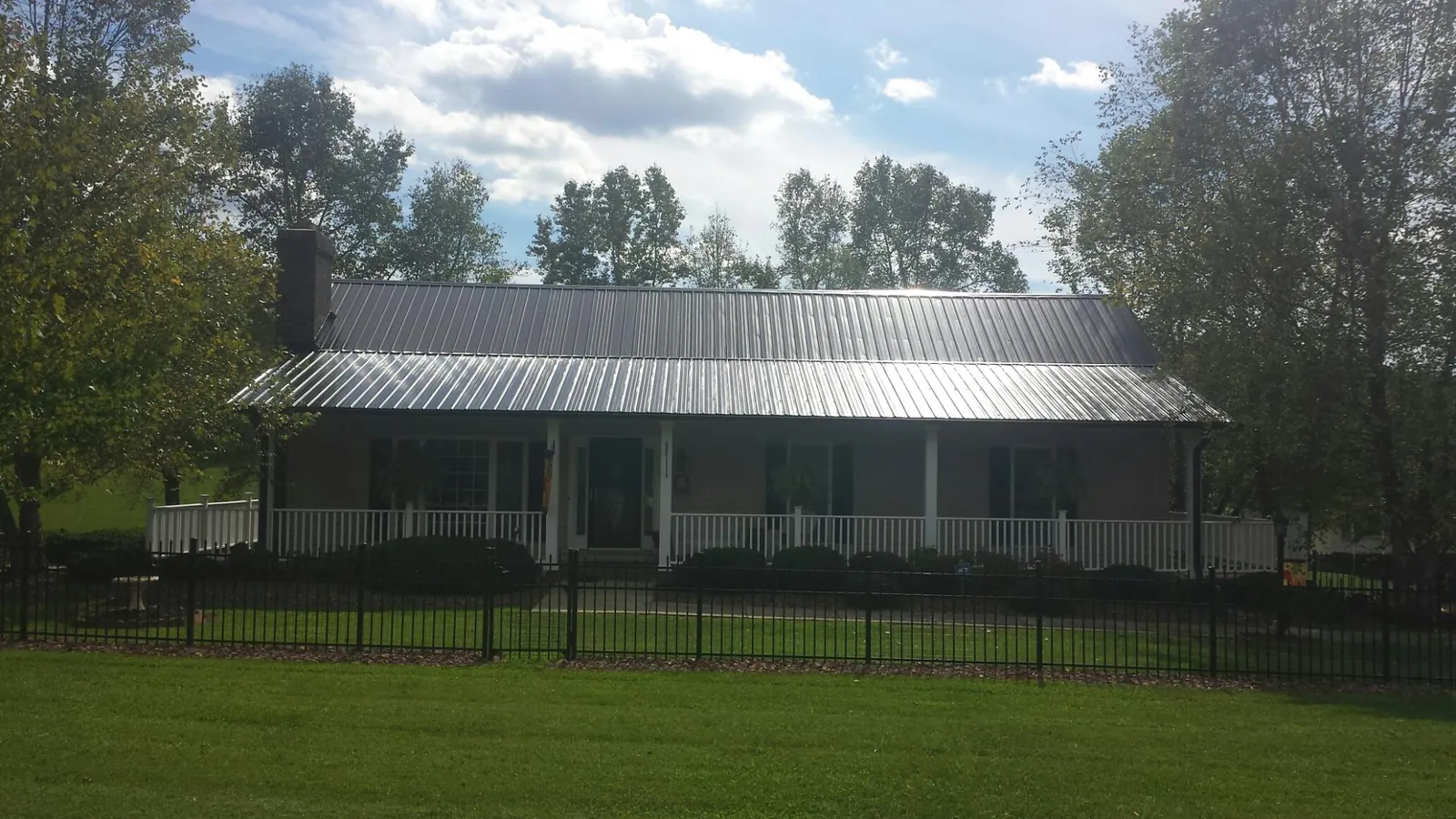 Gray metal roof on a brick ranch with a full width front porch — Gutter Guard Installation work by our crew in Sweeny