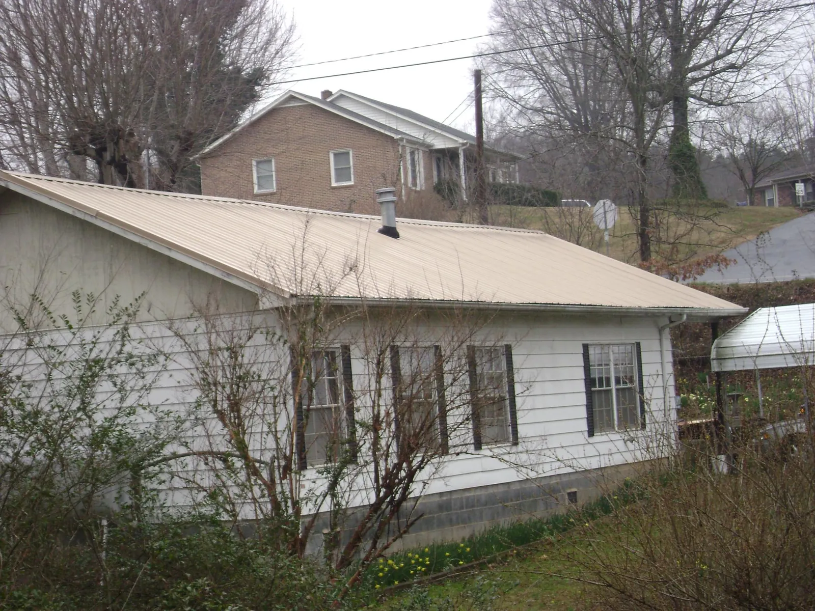 Tan metal roof on a white sided house set into a hillside — Commercial Roofing by Roofing Brothers in Sweeny