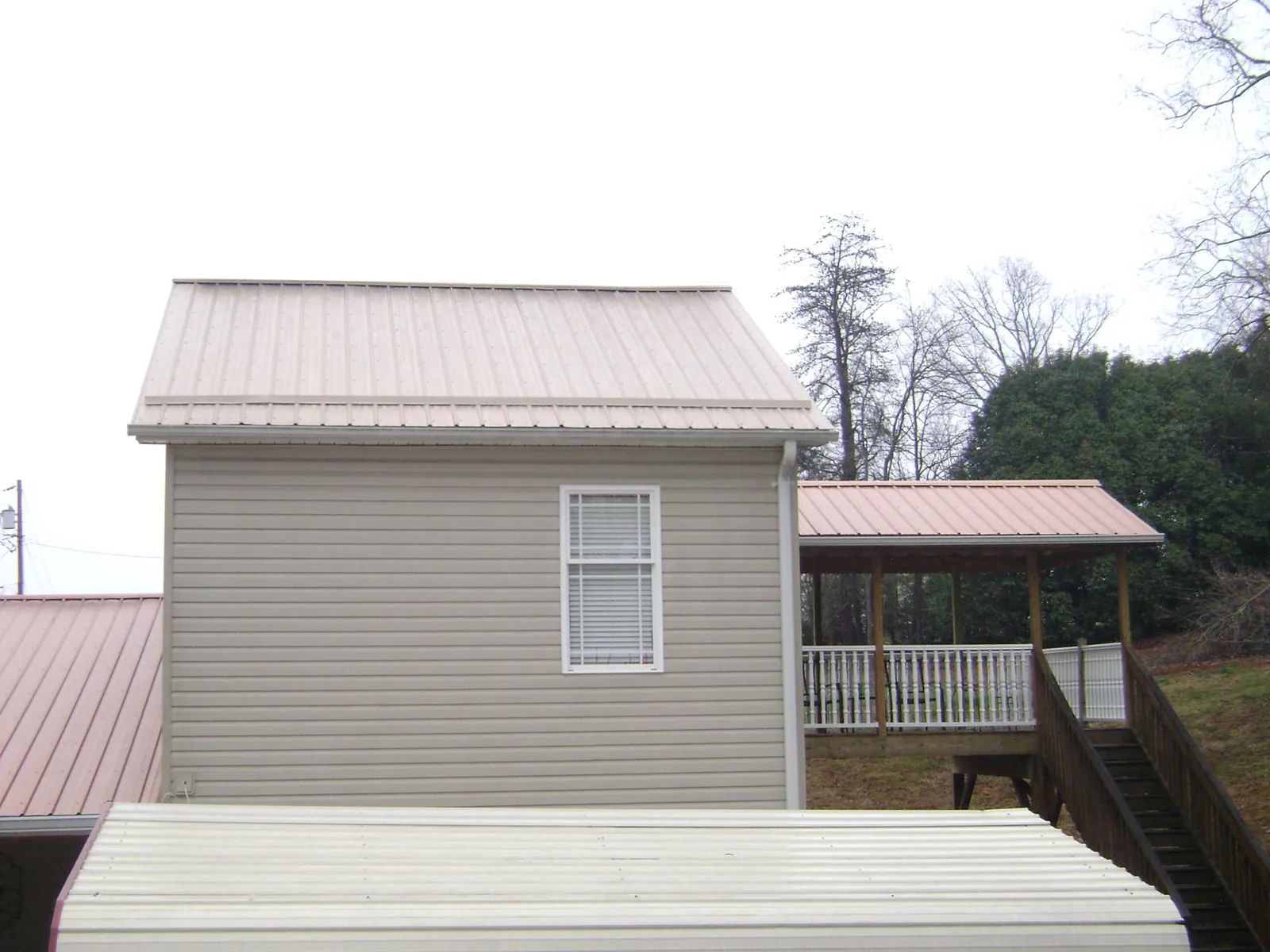 Tan metal roofs on a two story addition and attached porch, from a Roof Replacement job in Sweeny